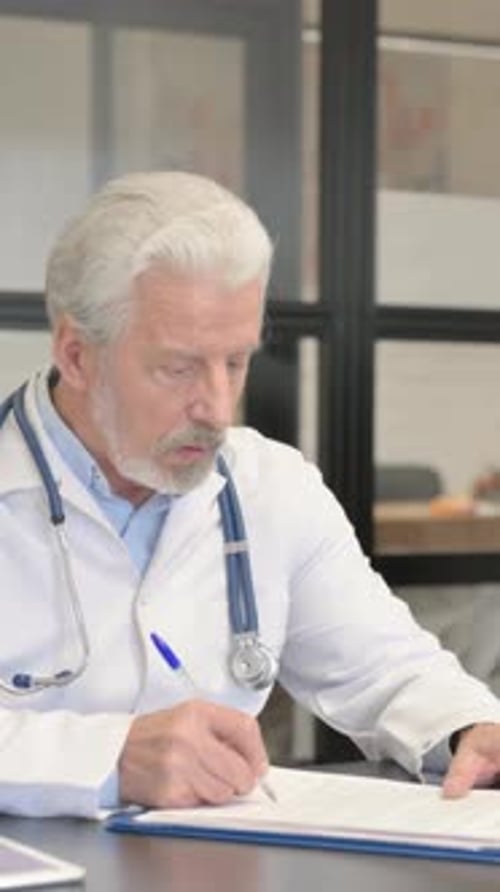 Senior Doctor Reviews Medical Records in Office