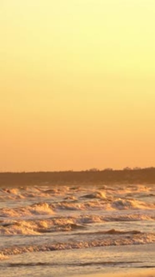 Orangefarbener Sonnenuntergang über dem Meer. Schäumende Meereswellen umspülen am Abend das sandige Ufer
.