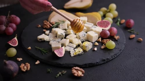 Woman Pours Honey Onto Sliced Traditional Italian Gorgonzola Cheese on Stone Seving Board