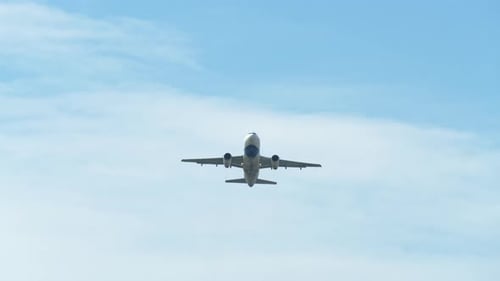 An airplane captured from its underside as it is taking off revealing a blue sky and clouds, airport