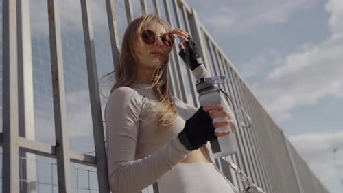 Sporty woman in activewear standing on street and drinking water after workout