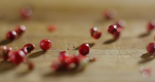 Dry Pink Peppercorns Falling onto Wooden Surface