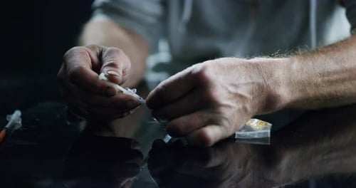 Hands, drugs and heroin with an addict closeup on a dark background to inject narcotics using