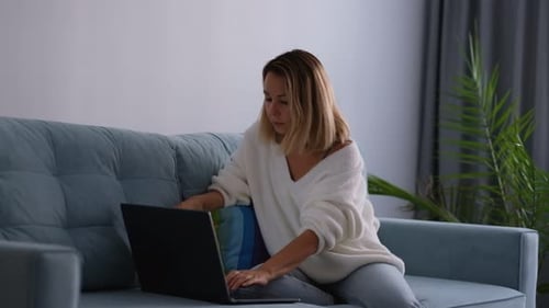 Smiling Woman Sitting with Laptop on Sofa in Lounge