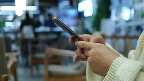Close up of woman's hand typing text on smartphone in cafe.