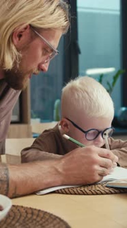 Father Helping Child Writing in Notebook at Home