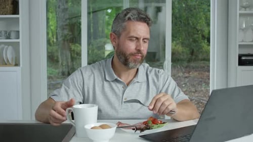 Man Having Breakfast While Watching Laptop Inside