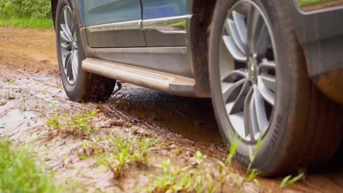 A close-up of a car passing through a dirt road in Argentina, navigating through a mud puddle.