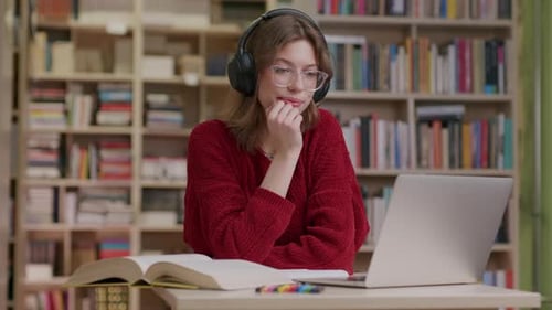 Young woman listening to audio using headphones in library