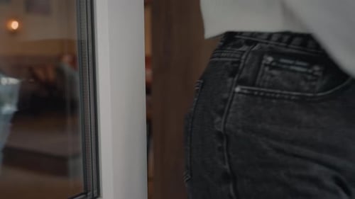 Lady in Jeans Exits Mall Holding Book with Hand on Glass Door Handle