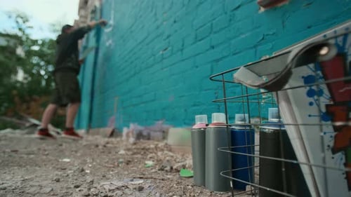 Pinturas de grafite e caderno de esboços no chão e homem pintando parede