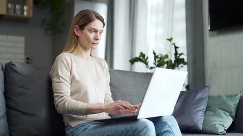 Woman Uses Laptop on Gray Couch Indoors