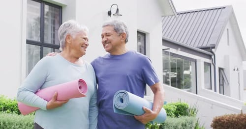 Portrait of happy senior diverse couple with yoga mats in garden