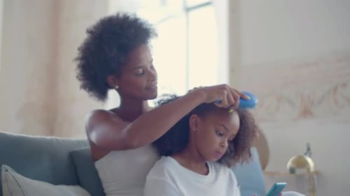 Woman Brushing Child's Hair While Using Phone