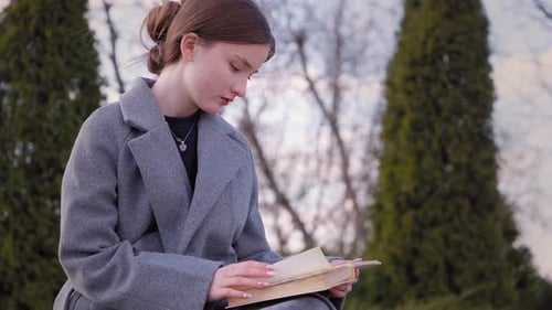 Young woman reading a book on a bench in a park