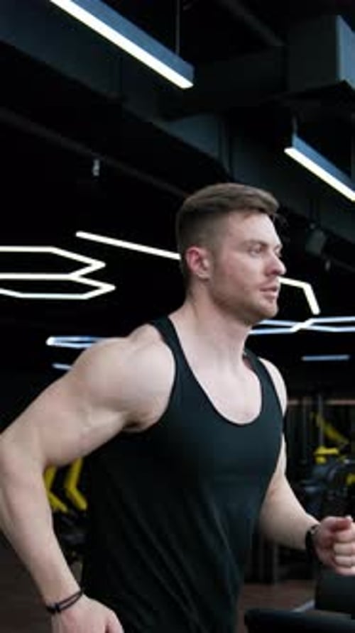 Homem bonito com um corpo treinado está correndo em uma esteira.