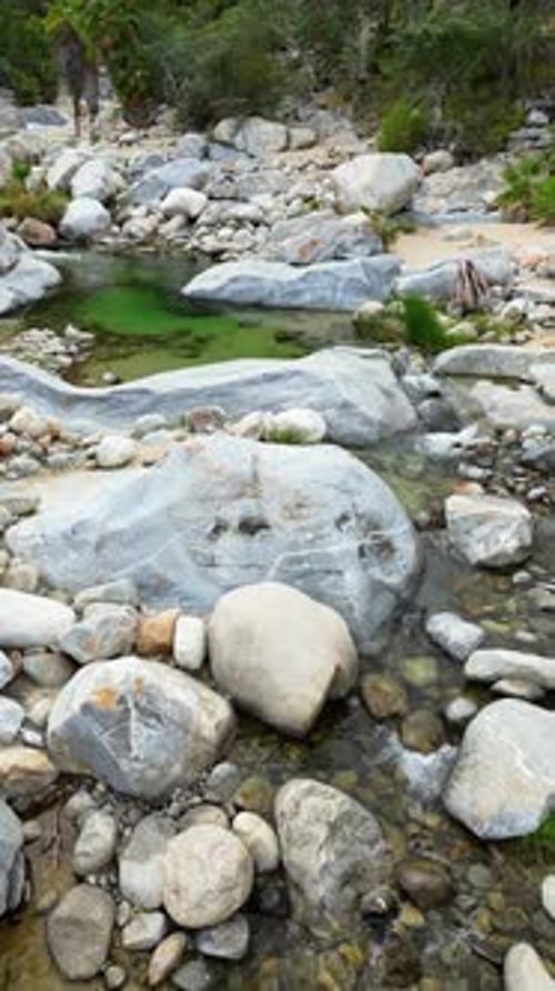 Aerial drone view of a small waterfall cascading between massive rocks into a natural pool in Baja C