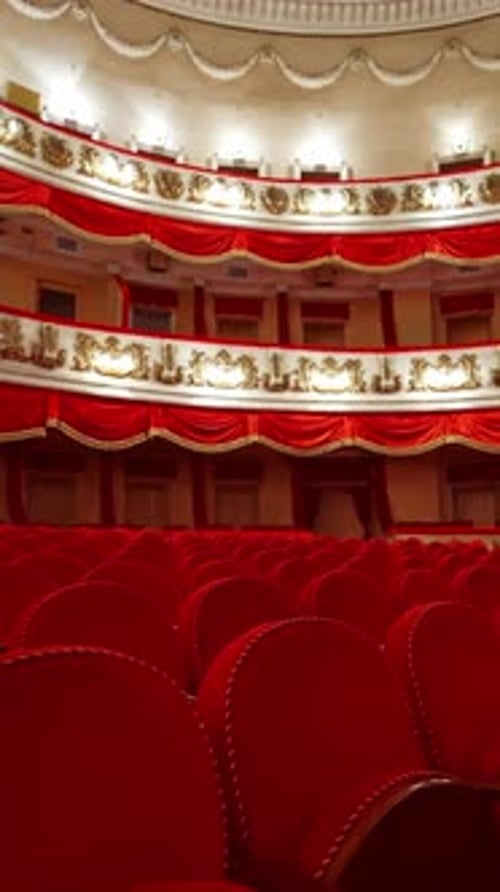 Panoramic view of beautiful richly decorated theater hall. Rows of red chairs in theater hall.