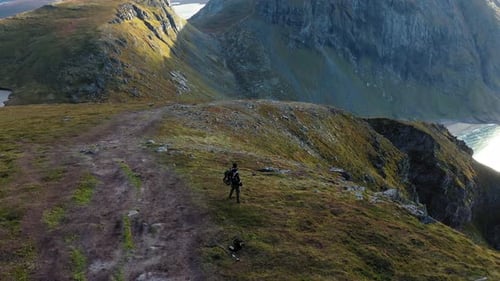 Epic rotating aerial footage of a hiker standing atop a mountain taking in the spectacular views fro