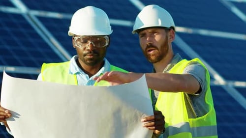 Portrait of Two Engineers with Project Plan on the Solar Farm in Special Uniform Standing Discuss