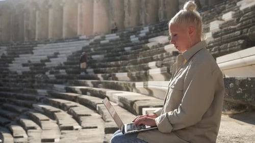 Eine junge Frau sitzt mit einem Laptop auf den Stufen eines antiken Amphitheaters