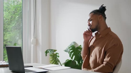 Young Man Thinks and Writes at Desk at Home