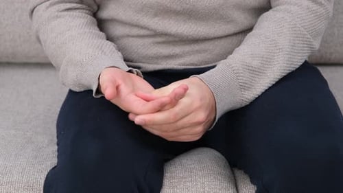Man Rubs Sore Hands on Couch