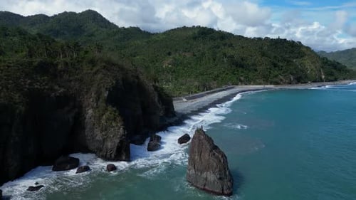 A drone shot reveals a small mountain next to the ocean, its rugged terrain contrasting with the cal