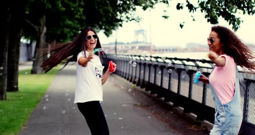 Two Women Blowing Bubbles in an Urban Park