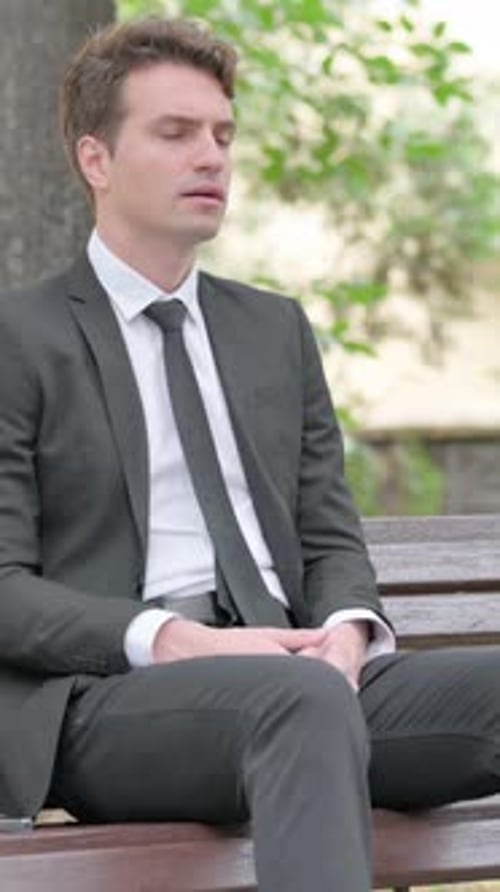 Stressed Man Rubbing Temples While Sitting on Bench