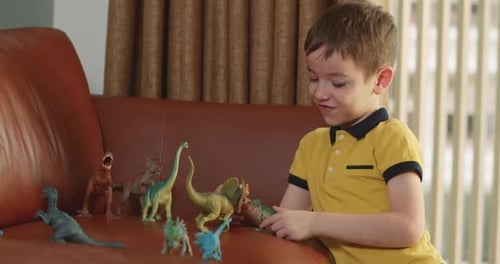 Child Plays with Dinosaurs on Couch at Home