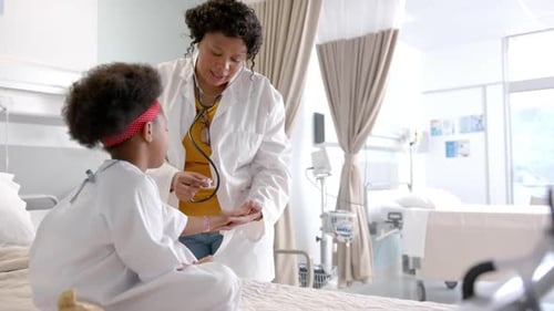 African american female doctor examining girl using stethoscope in hospital room, slow motion
