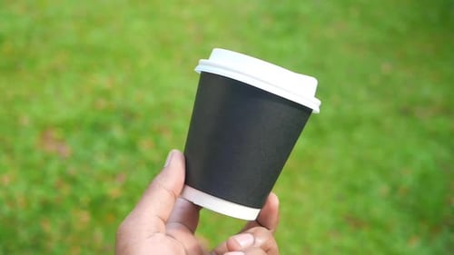 Hand Holds Coffee Cup on Green Background