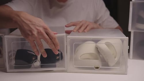 Closeup Front View of Young Man Organizing and Storing Seasonal Shoes in Clear Plastic Containers