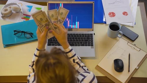 Woman Watches Stock Chart at Desk with Money