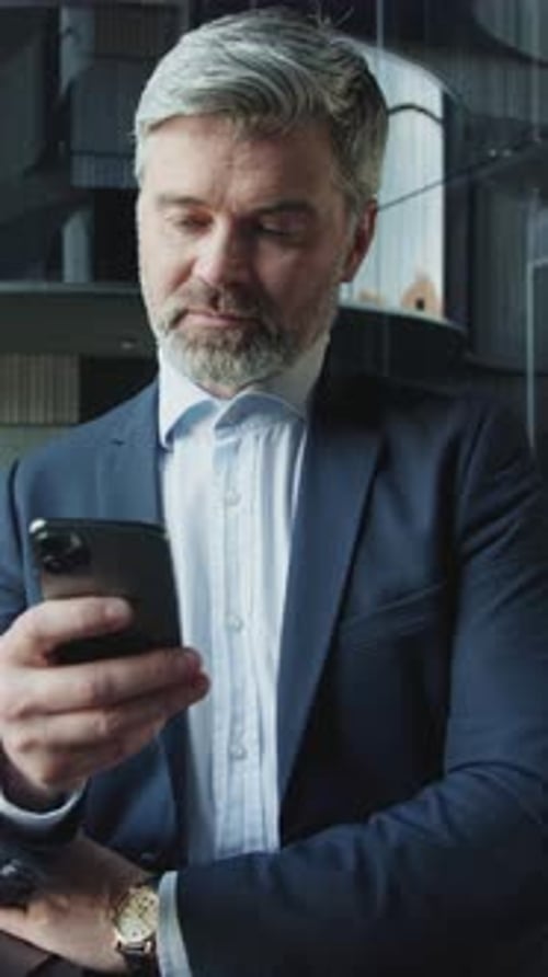 Shot of Confident Caucasian Middleaged Businessman in Elegant Suit Looking at Screen of Smartphone