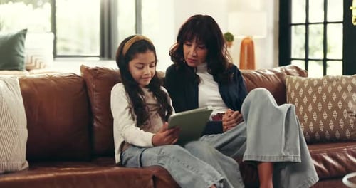 Mother and Daughter Use Tablet on Couch Indoors