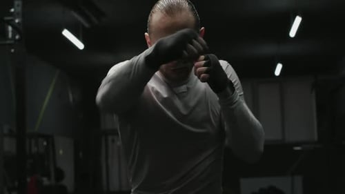 Martial Arts Sportsman in Grey Training Suit Boxing at Camera in Closeup Against Dark Gym Interior