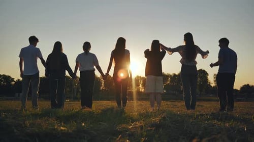 Siete amigos hacen una forma de corazón con sus manos al atardecer