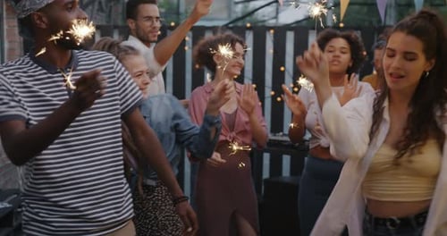 Group of Young People Dancing with Bengal Lights Outdoors in Street Cafe Enjoying Music in Summer