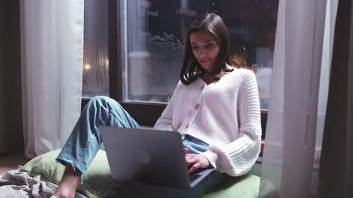 Young Woman Freelancer is Sitting on the Floor and Working on a Laptop Evening Time Remote Work From