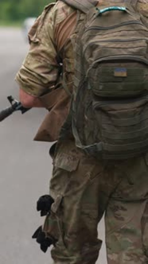 Ein Mitglied der Streitkräfte mit einer Schusswaffe und einem Rucksack rückt die Straße entlang vor