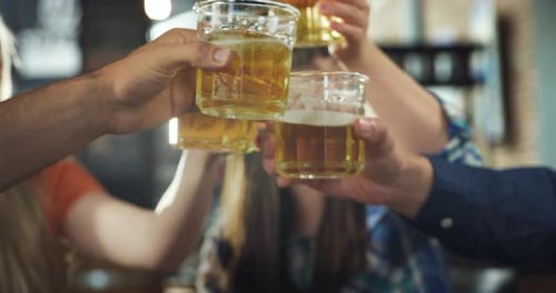 Close Up on Clinking Glasses with Beers Held by Young Friends Celebrating During Day Tim