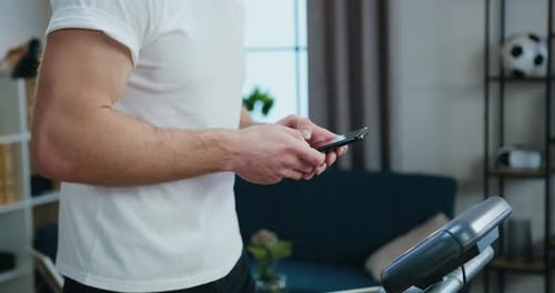 Man Using Phone While Standing on Treadmill Indoors