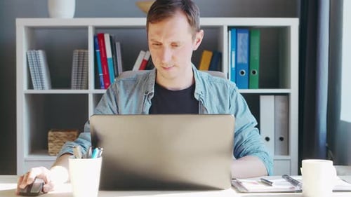 Junger männlicher Unternehmer arbeitet im Home-Office am Computerarbeitsplatz eines Freiberuflers oder Studenten