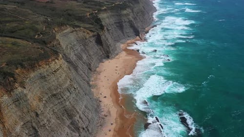 Waves Crash Against Rugged Cliffs Beside Sandy Beach