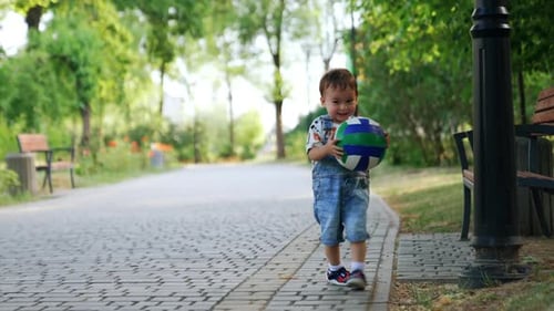 Smiling toddler boy throwing a ball happily. Adorable Caucasian child playing in the park in summer.