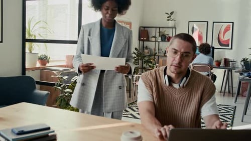 Black Woman Walking Up to her Colleague to Show him Paper Document in Office