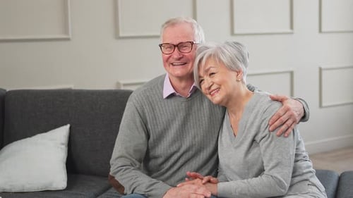 Loving Elderly Couple Embrace on Sofa Indoors