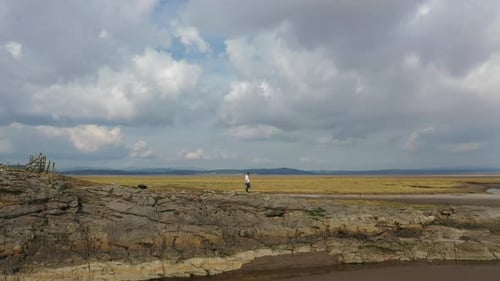 Aerial wide shot of a person walking along the rocks on a shore line at low tide, on bright summers